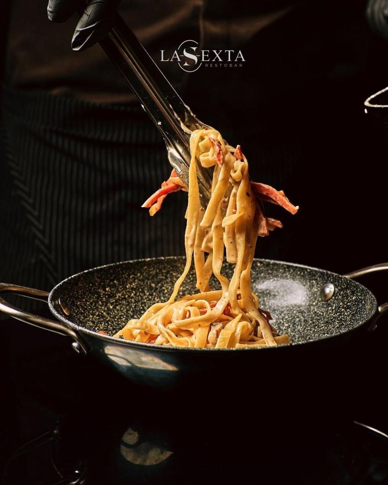 Fettuccine levantado con pinzas de un sartén, con tiras de tocino.