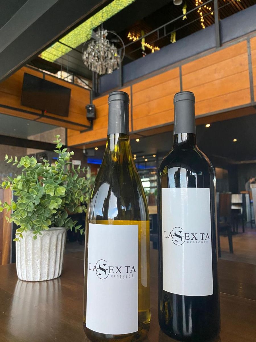 Dos botellas de vino con etiqueta de La Sexta Restobar sobre una mesa de madera.